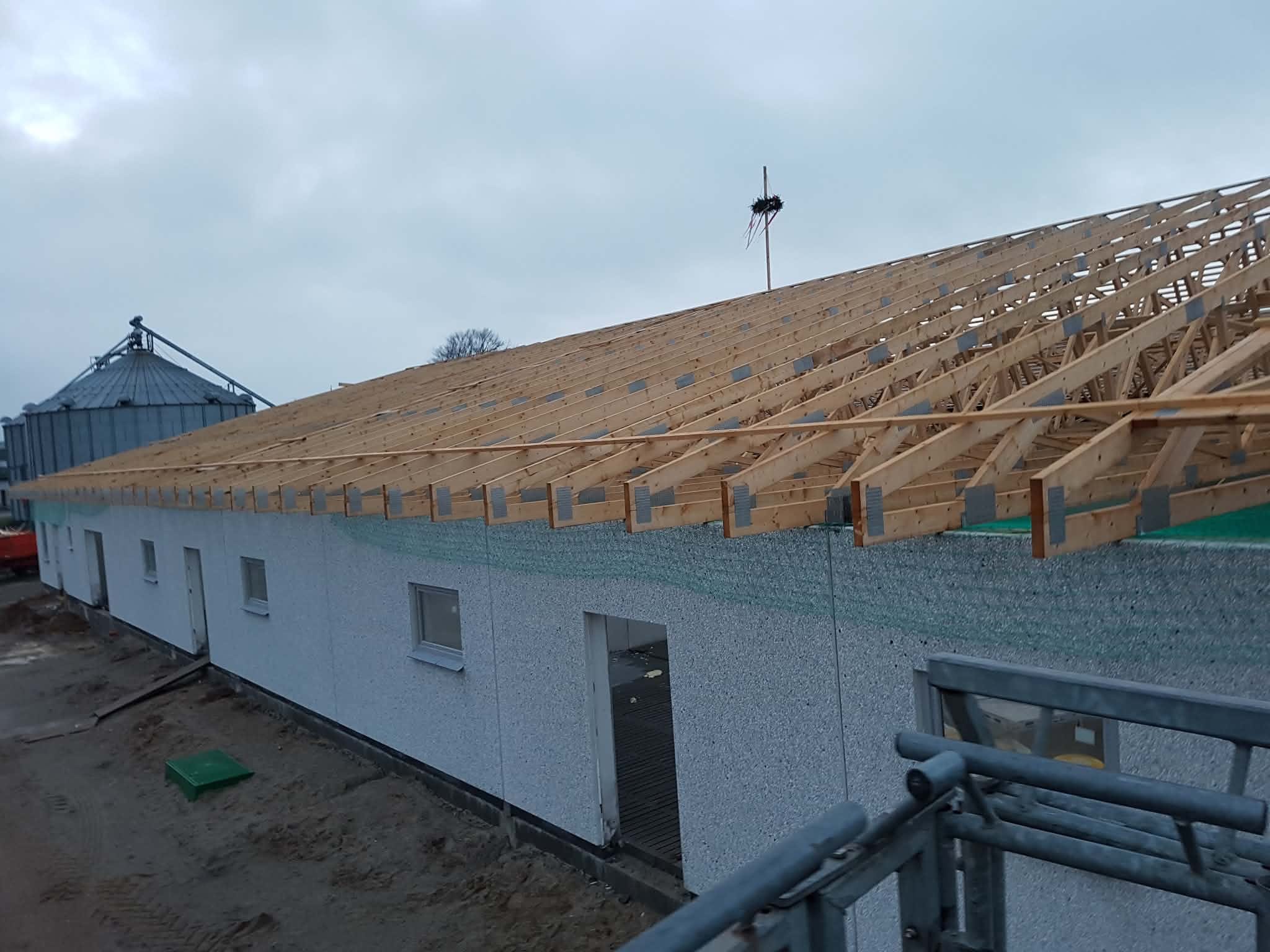 Buitenaanzicht van een lang gebouw met geplaatste houten dakspanten