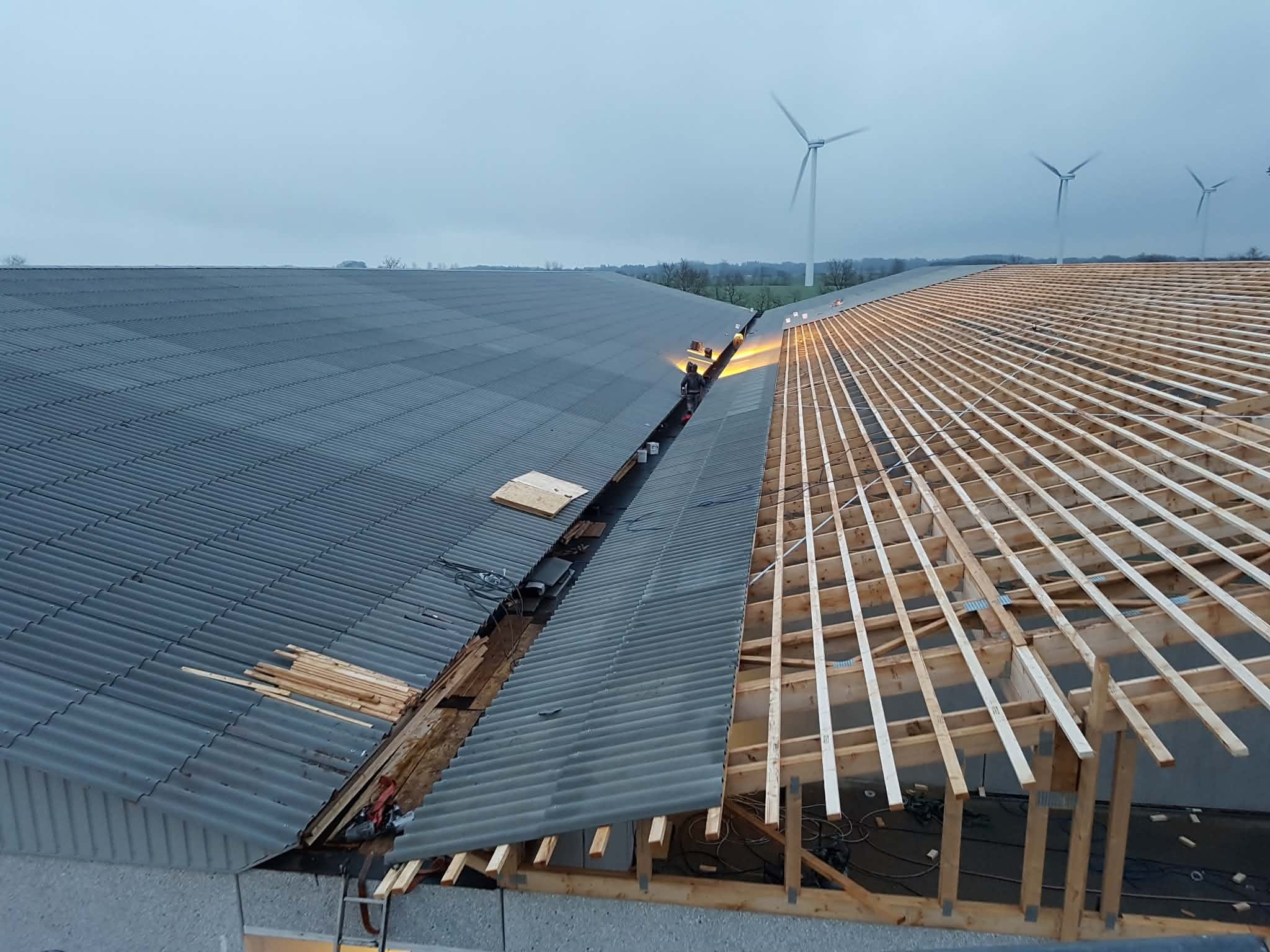 Groot bedrijfsdak tijdens renovatie: golfplaten links, nieuwe houten dakstructuur rechts