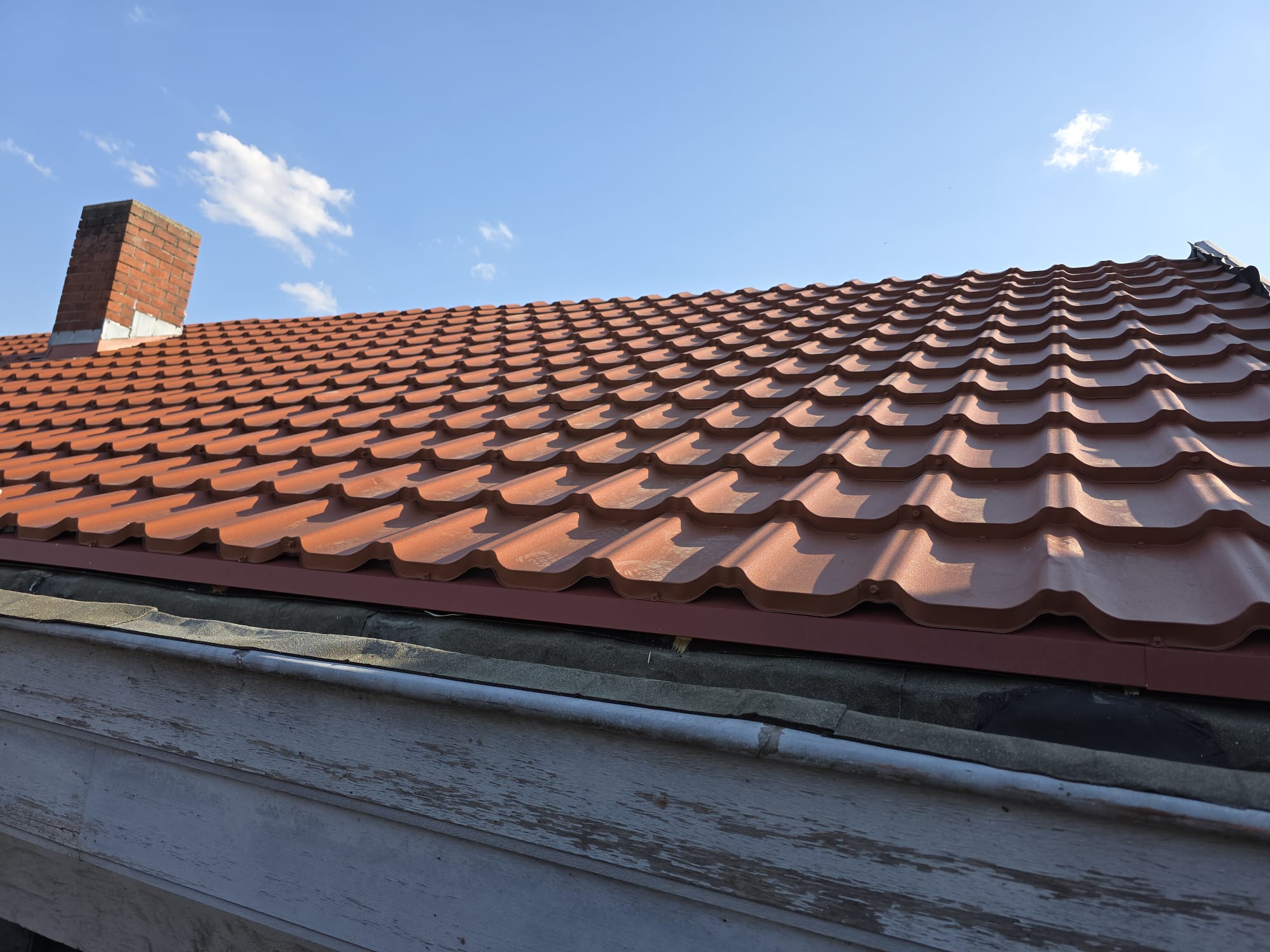 Strak terracotta pannendak met dakgoot en bakstenen schoorsteen